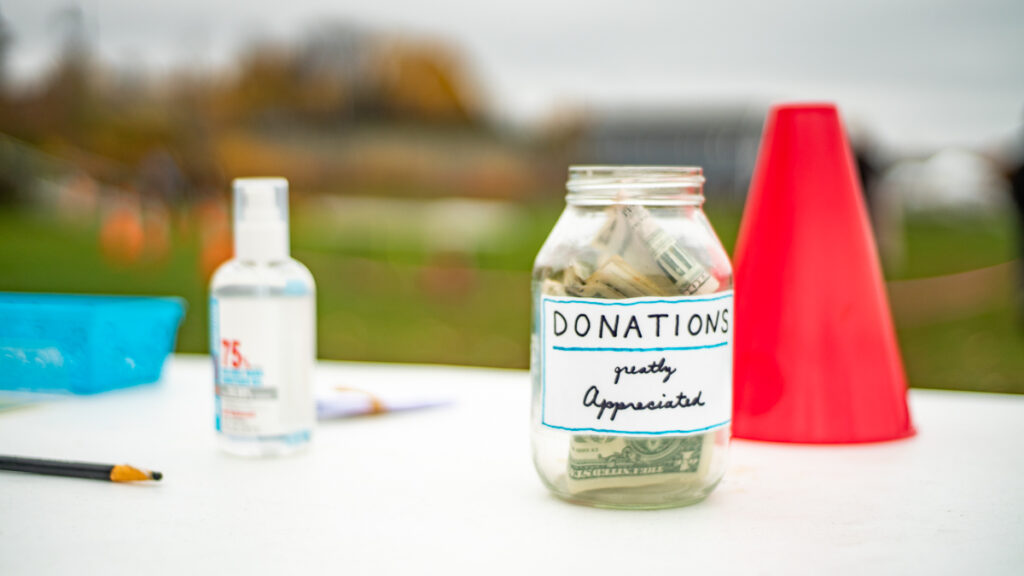 A close-up of a glass tip jar with a label that says Donations Greatly Appreciated that is filled with cash.