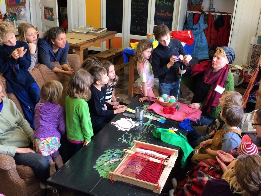 A group of children and parents sgathered around a colorful table and their teacher.